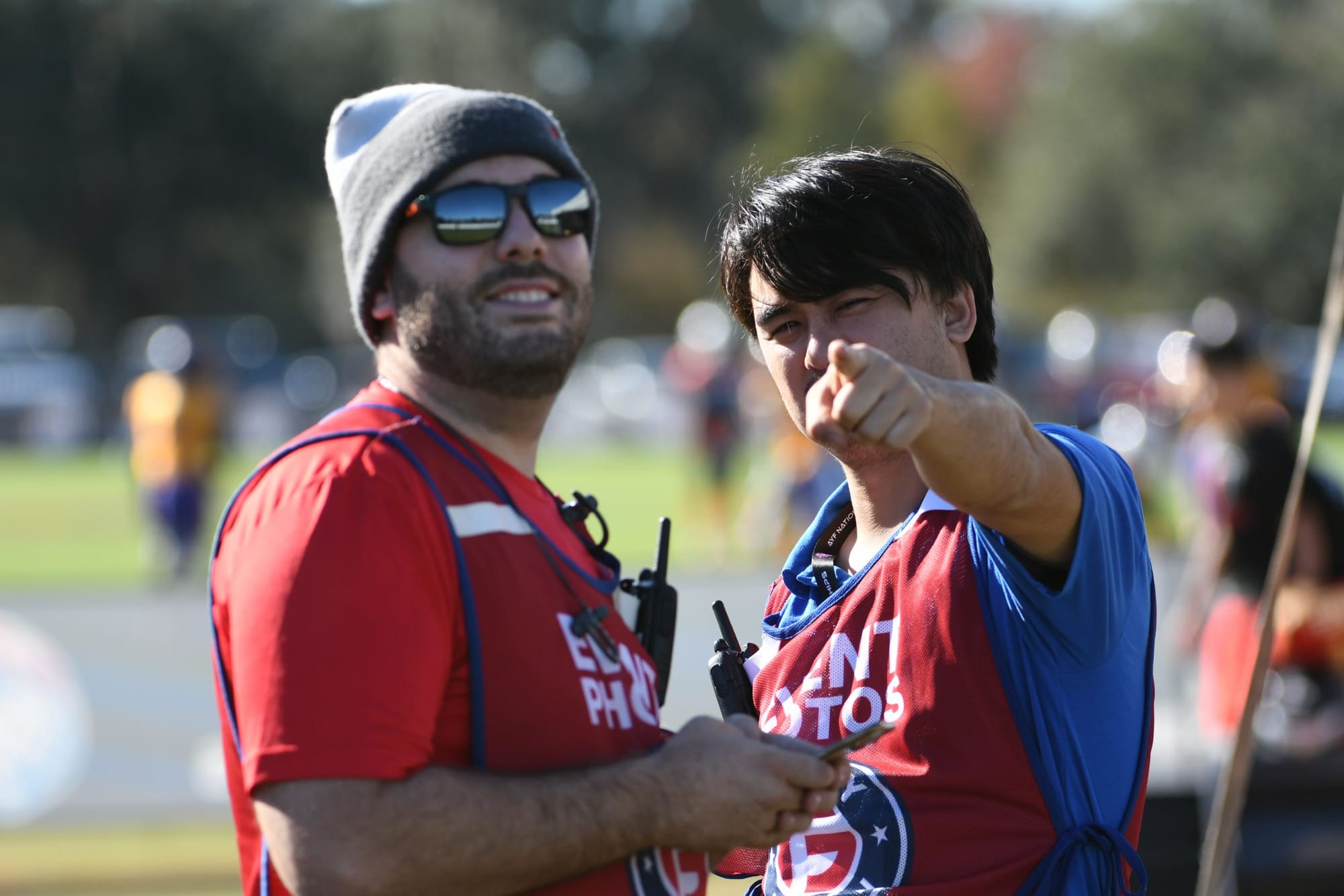 Two crew members on the sideline, one pointing out the action