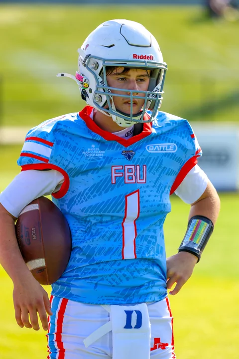 Quarterback in light blue holding the ball on the sideline