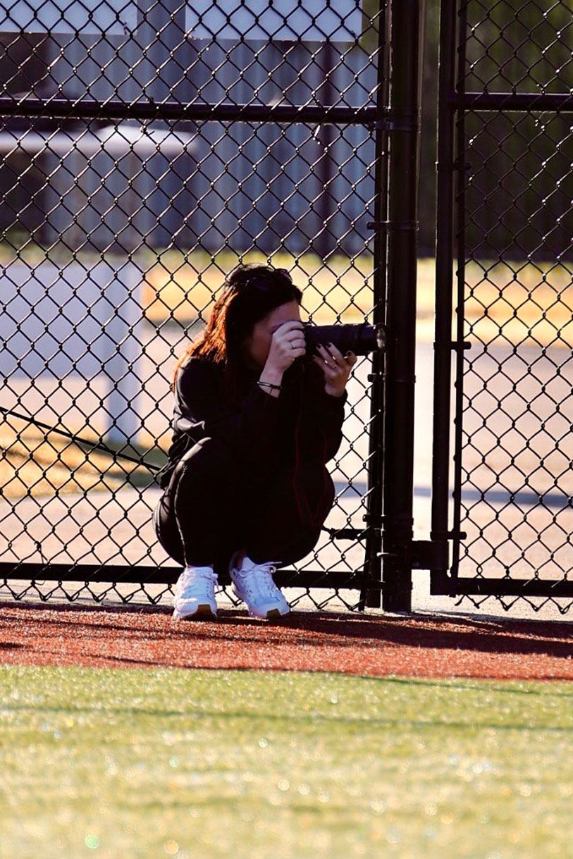 A parent crouching with a camera inside the field fence